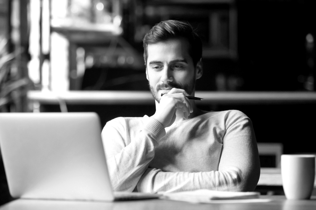 A man looks thoughtfully at a laptop